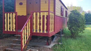 A small, single-story wooden structure with a porch and steps leading to a door. - Caravan (Arles)