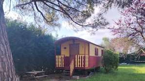 A stationary train car with a small porch and a picnic table nearby. - Caravan (Arles)