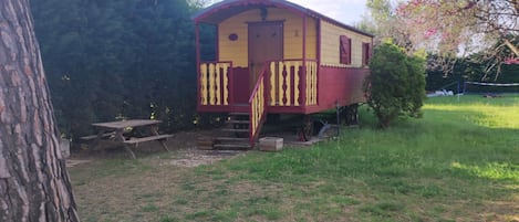 A stationary train car with a small porch and a picnic table nearby.