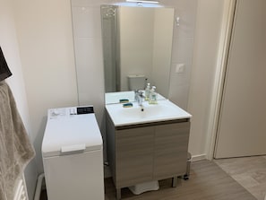 Een moderne badkamer met een wit wastafel, spiegel en een compacte wasmachine.