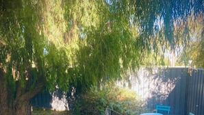 Un patio con un árbol, una banca de metal y una mesa con sillas.