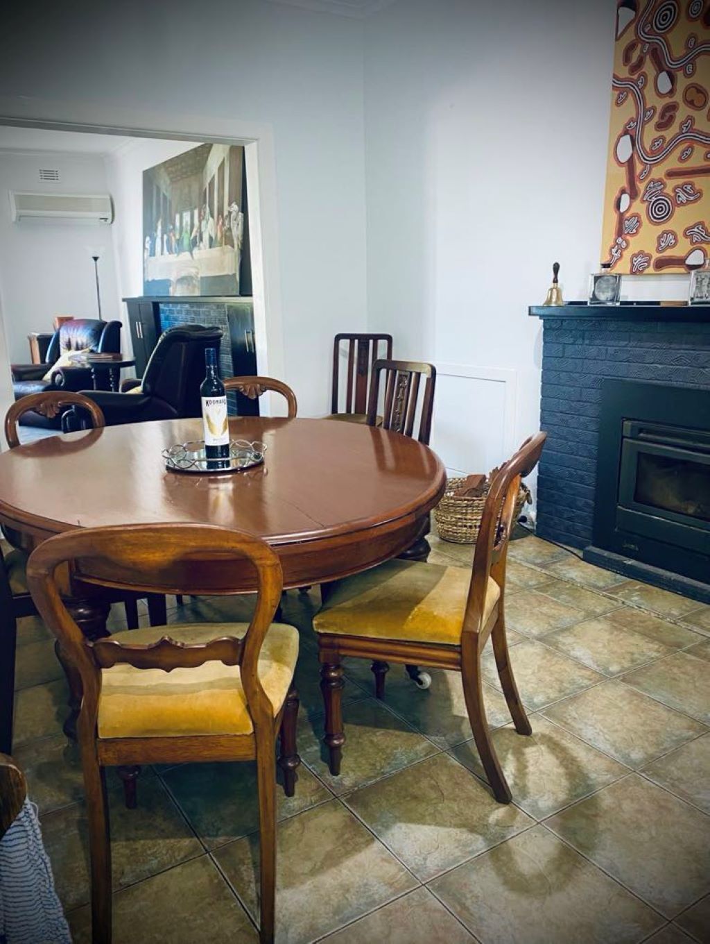 A dining room with a round wooden table and six chairs, a fireplace, and a patterned wall.