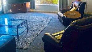 Una sala de estar con televisor, sofá, mesa de centro y un ventanal con cortinas.