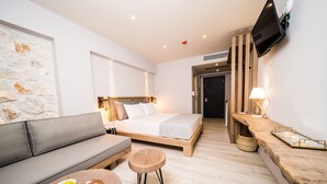 Una habitación de hotel moderna con una cama, un sofá, una mesita redonda y un televisor montado en la pared.