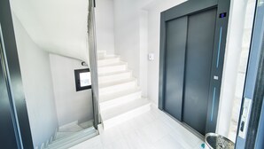Un interior moderno con una escalera blanca, un panel digital de ascensor y una barandilla de metal.