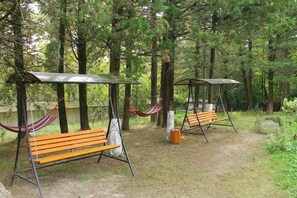 Two wooden swing benches with metal frames, a hammock, and a covered seating area in a forest setting.