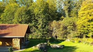 Eine rustikale Holzhütte mit einem Ziegeldach, umgeben von einem üppigen grünen Rasen und dichtem Wald.
