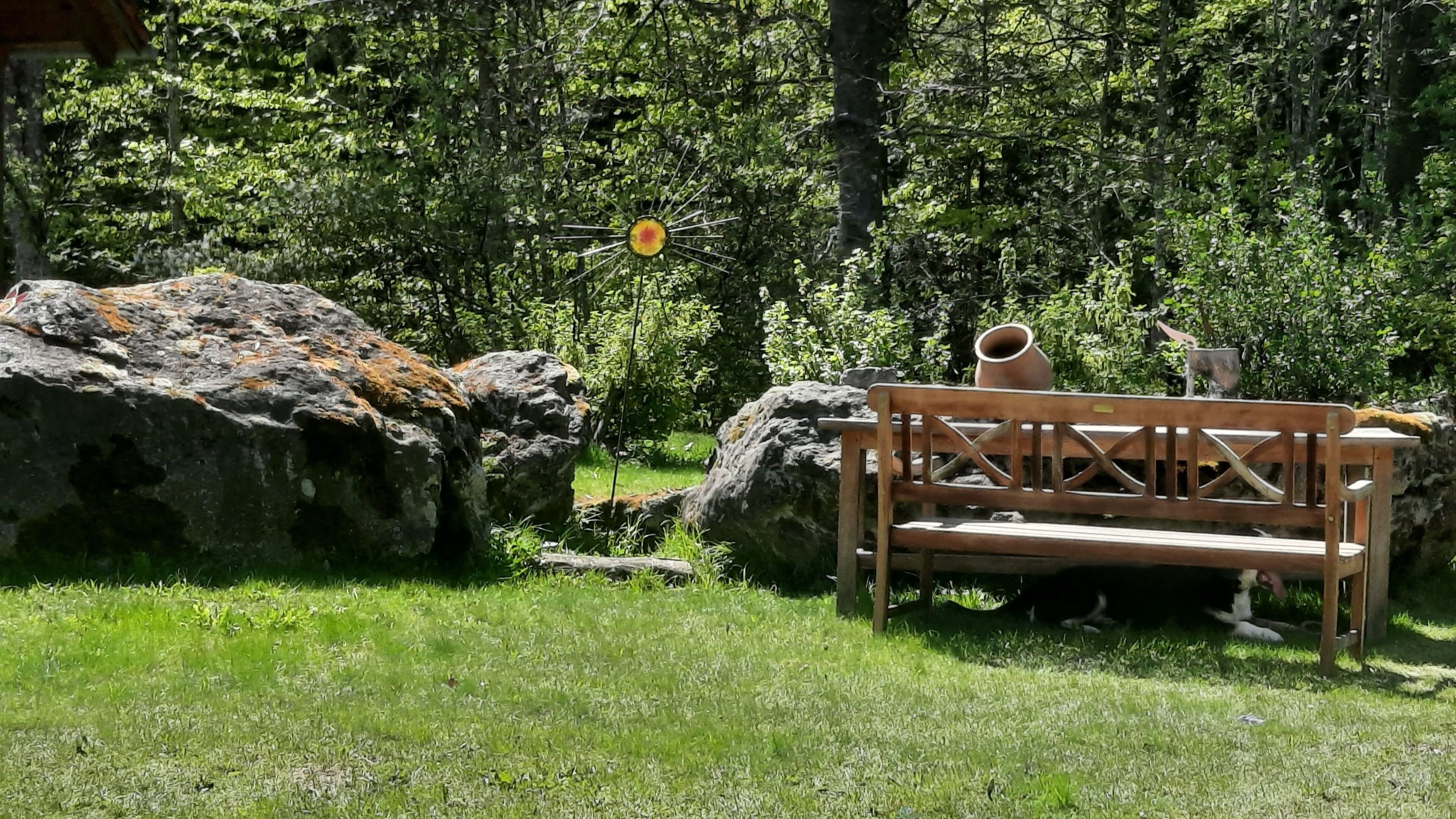 Un banc de fusta en una zona verda amb una roca i una test.