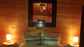 Ein Zimmer in einer Holzhütte mit einem Bett, zwei Nachttischlampen, einem Spiegel und einer Pendelleuchte.
