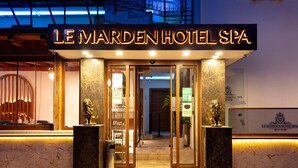 Exterior do Hotel Spa Le Marden, com placa visível, entrada em mármore e duas estátuas de leão.