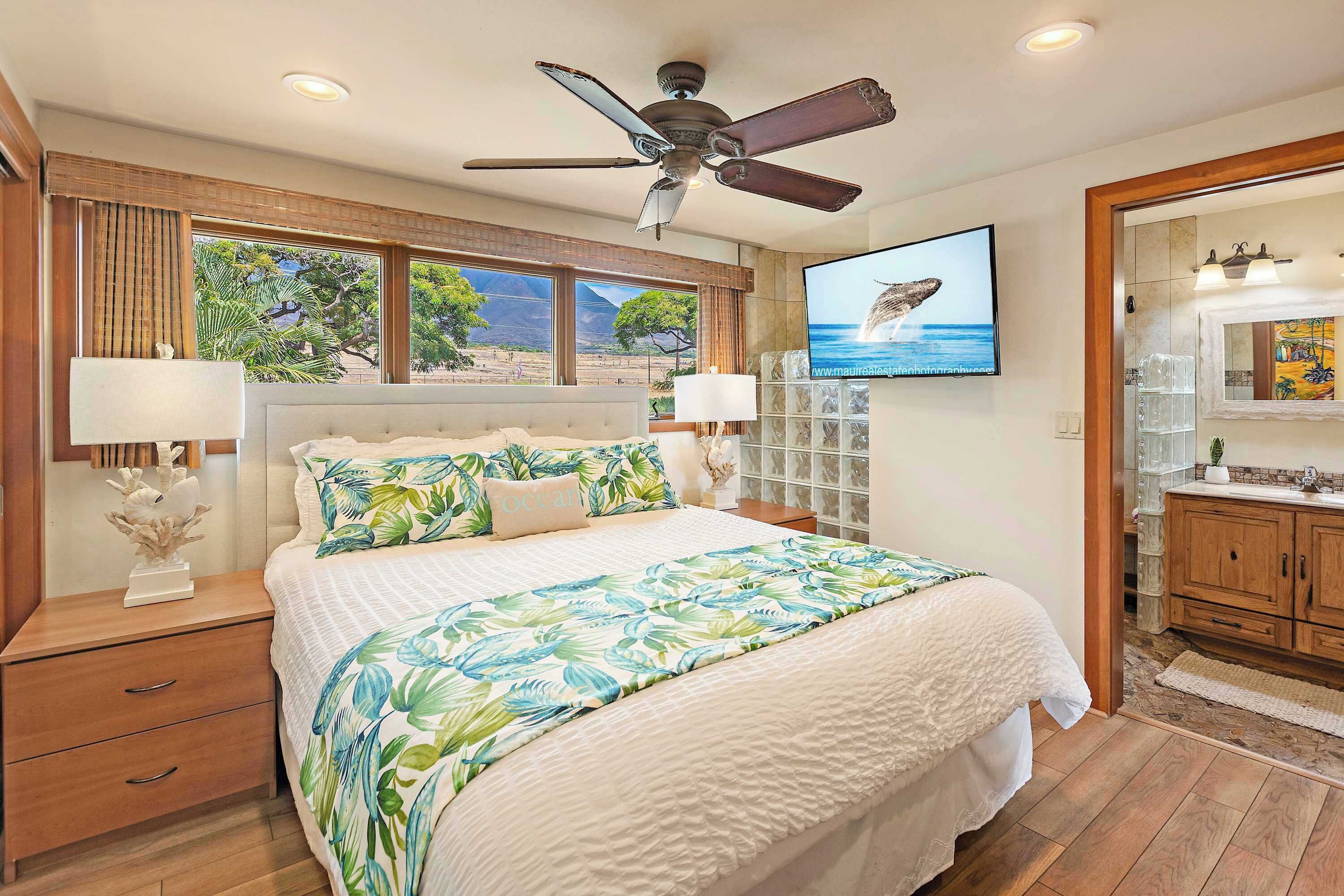 A bedroom with a bed, nightstands, a ceiling fan, a TV, and a view of the outdoors.