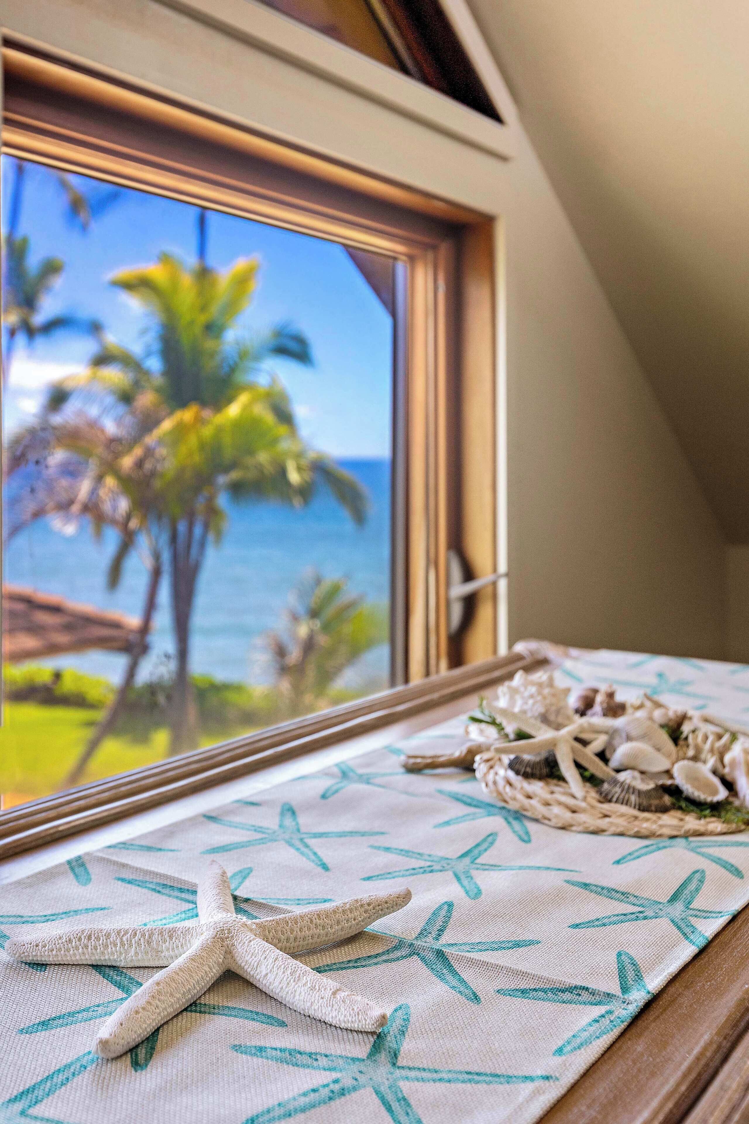 Una estrella de mar sobre una mesa, una cesta tejida con conchas y vista a palmeras y al océano a través de una ventana.