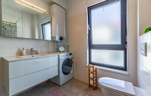 Ett modernt badrum med tvättmaskin, toalett, ett stort spegel och ett fönster.
