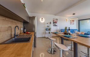 Ett modernt kök med en bänkskiva i trä, rostfria köksapparater och en matplats med en blå soffa och ett bord för två personer.
