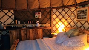 A cozy room with a bed, a small wooden desk, and a wall-mounted shelf with various items. - Bembridge Harbour Yurt - Log Burner - Wifi (Ryde)