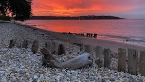 A pebbled beach with wooden posts and driftwood, overlooking a calm sea during sunset. - Bembridge Harbour Yurt - Log Burner - Wifi (Ryde)