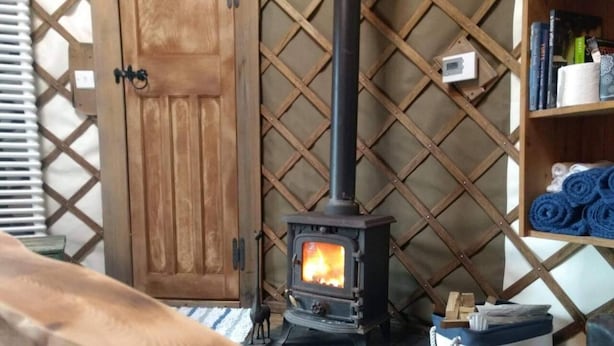 A room with a wood-burning stove, a wooden door, and a shelf with rolled towels. - Bembridge Harbour Yurt - Log Burner - Wifi (Ryde)