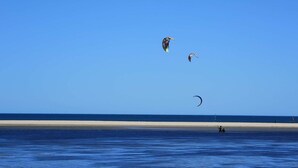 Une plage avec un ciel dégagé et trois cerfs-volants qui volent.