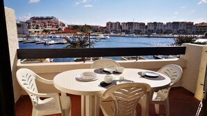 Un balcon avec une table et des chaises donnant sur une marina où l’on peut admirer des bateaux et des bâtiments.
