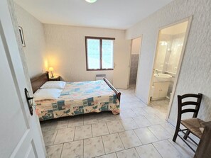 Ein Schlafzimmer mit Bett, Nachttisch, Fenster und einem Badezimmer mit Waschbecken sowie einem Sessel.