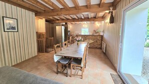 Ein gemütlicher Essbereich mit einem langen Holztisch und Stühlen, eine Küche im Hintergrund und ein großes Fenster mit Blick ins Freie.