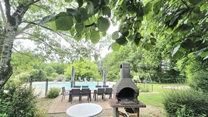 Eine Terrasse im Freien mit einem Steintisch und -stühlen, einem Backofen aus Ziegeln und einem Pool im Hintergrund.