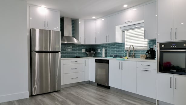 Una cocina moderna con armarios blancos, electrodomésticos de acero inoxidable y un salpicadero color turquesa.