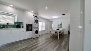 Una cocina moderna con muebles blancos, lavadora y secadora integradas, y un comedor con mesa y sillas blancas.