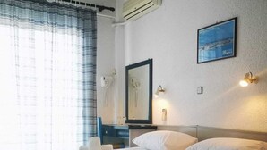 Ein Hotelzimmer mit zwei Betten, einem großen Fenster mit Vorhängen, einer Wand-Klimaanlage, einem gerahmten Bild an der Wand und einer Nachttischlampe.