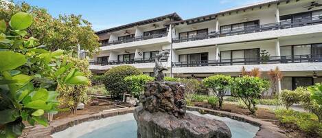 A hotel with a courtyard featuring a rock fountain, surrounded by greenery and a multi-story building with balconies.