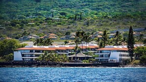 A coastal hotel with multiple buildings, some with red roofs, and palm trees in the foreground.