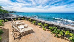 A beachside lounge with wooden loungers and a stone wall, overlooking the ocean.