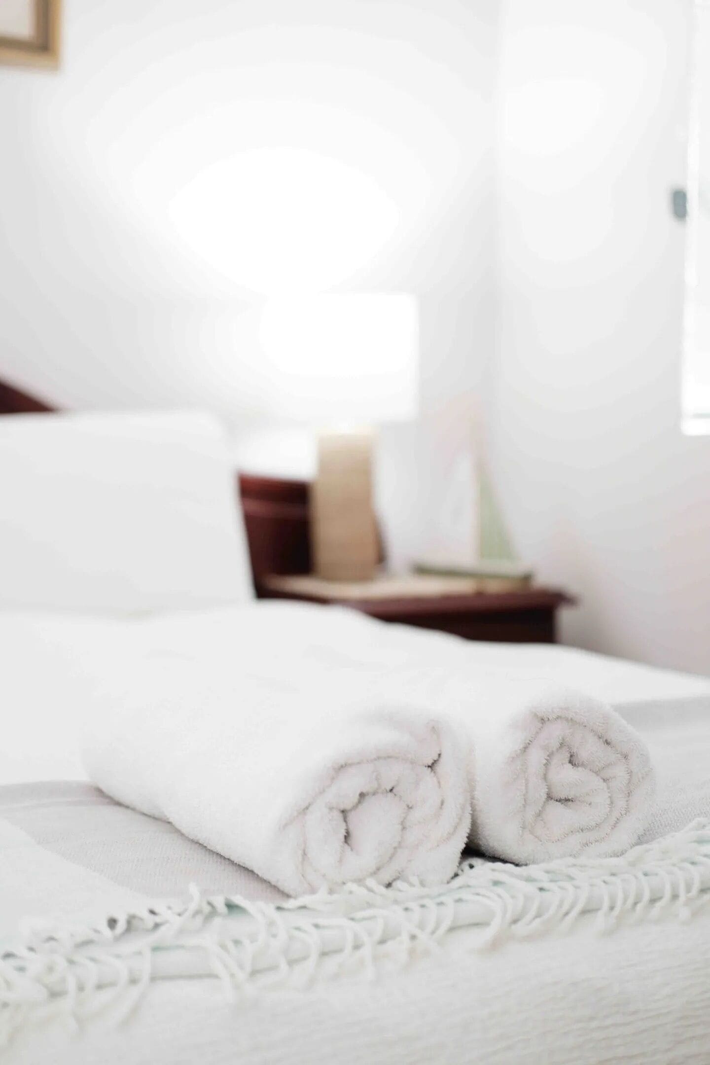 A neatly made bed with rolled white towels and a white throw blanket.