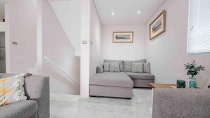 Ein modernes Wohnzimmer mit grauem Sofa, grauem Sessel und einer Treppe, die zu einer oberen Etage führt.