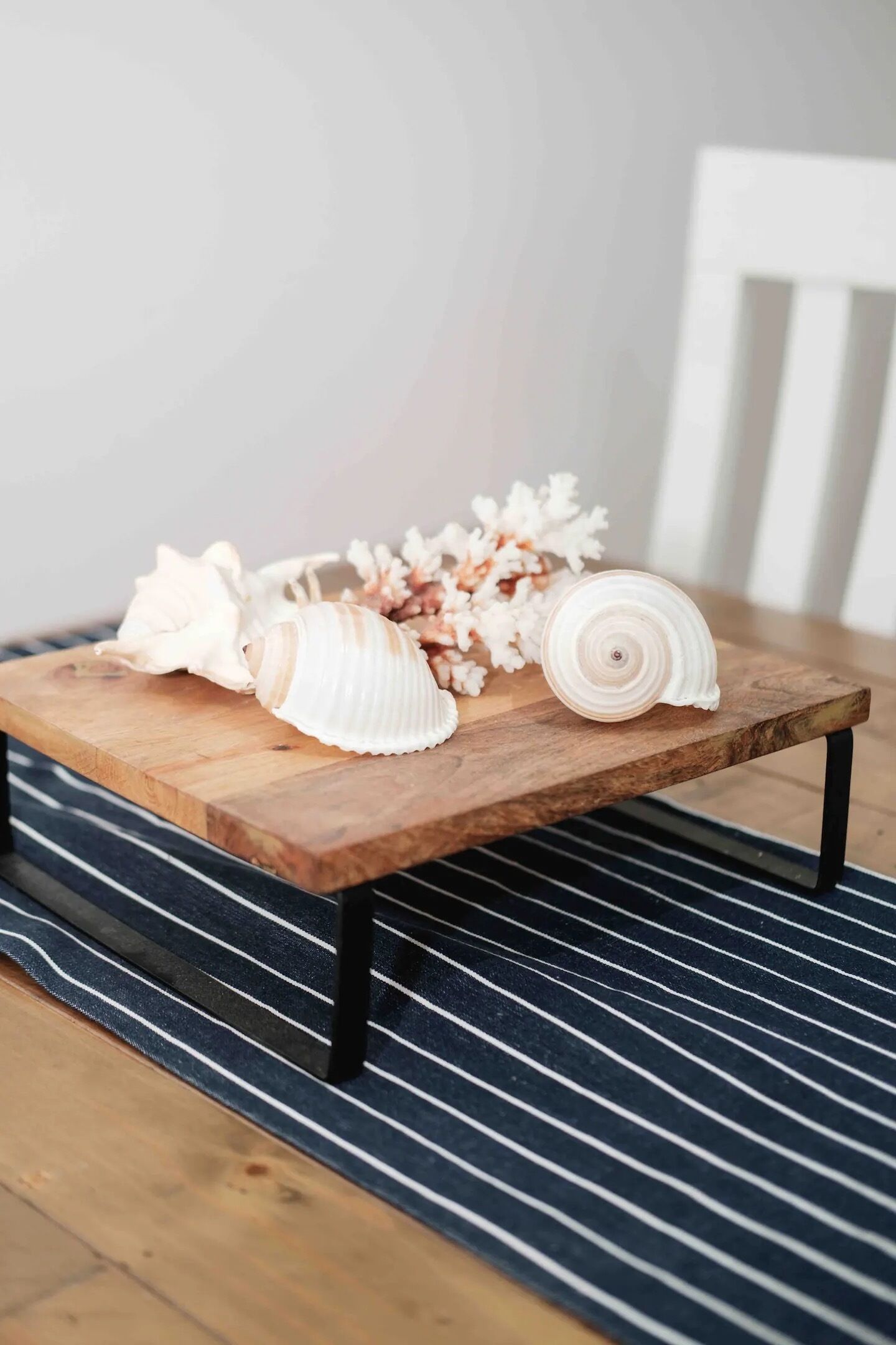 Un tavolo di legno con conchiglie e fiori secchi, su un tappeto a righe.