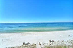 Une plage de sable blanc, avec une eau d’un bleu limpide et quelques constructions visibles au loin.