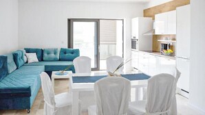 A modern apartment with a teal sofa, white dining chairs, a glass dining table, and a kitchen with white cabinets. - 2 bedroom lovely apartment in Sibenik (Sibenik)