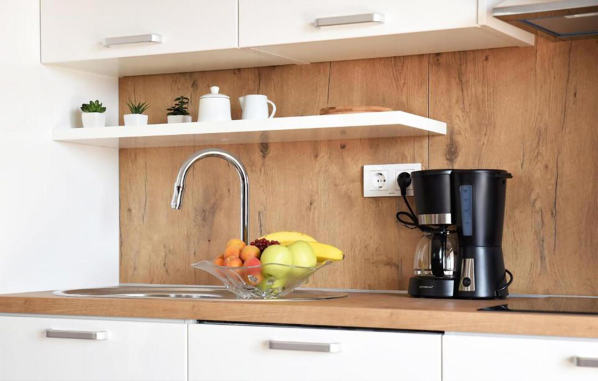 Una cocina moderna con protector contra salpicaduras de madera, un lavamanos de acero inoxidable, una cafetera y un frutero.
