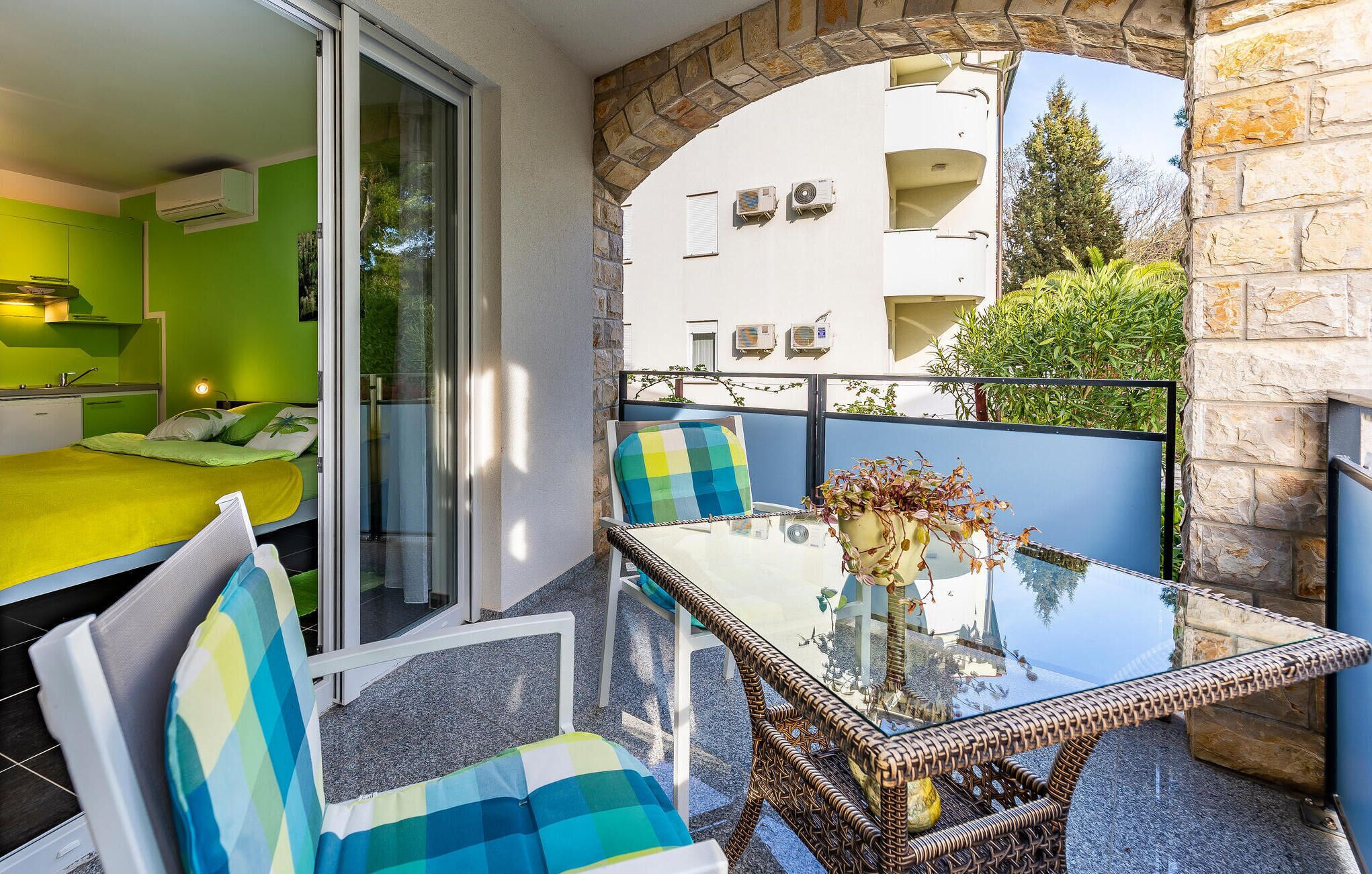 A balcony with a glass table, wicker chairs, and a view of a pool and buildings.