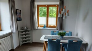 Ein Essbereich mit Tisch, Stühlen, einer Zimmerpflanze und einem Fenster mit Vorhängen.