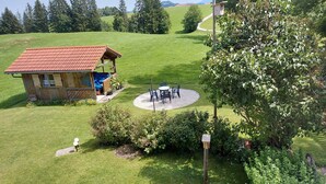 Ein rustikales Holzhaus mit rotem Dach, einer Terrasse mit Sitzgelegenheiten und einem gepflegten Rasen.