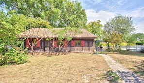 A rustic wooden house with a tiled roof, surrounded by a grassy yard and trees.
