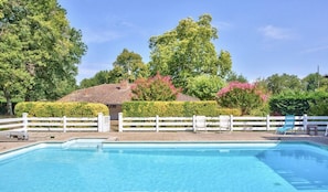 A swimming pool with a white fence, lounge chairs, and a building with a tiled roof in the background.