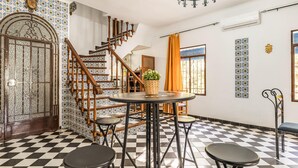 Une pièce dotée d’un sol à carreaux, d’un escalier avec des rampes en bois, d’une table ronde entourée de tabourets et de murs aux motifs décoratifs.