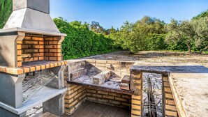 Un espace barbecue extérieur en briques, doté d’une cheminée et entouré de verdure.