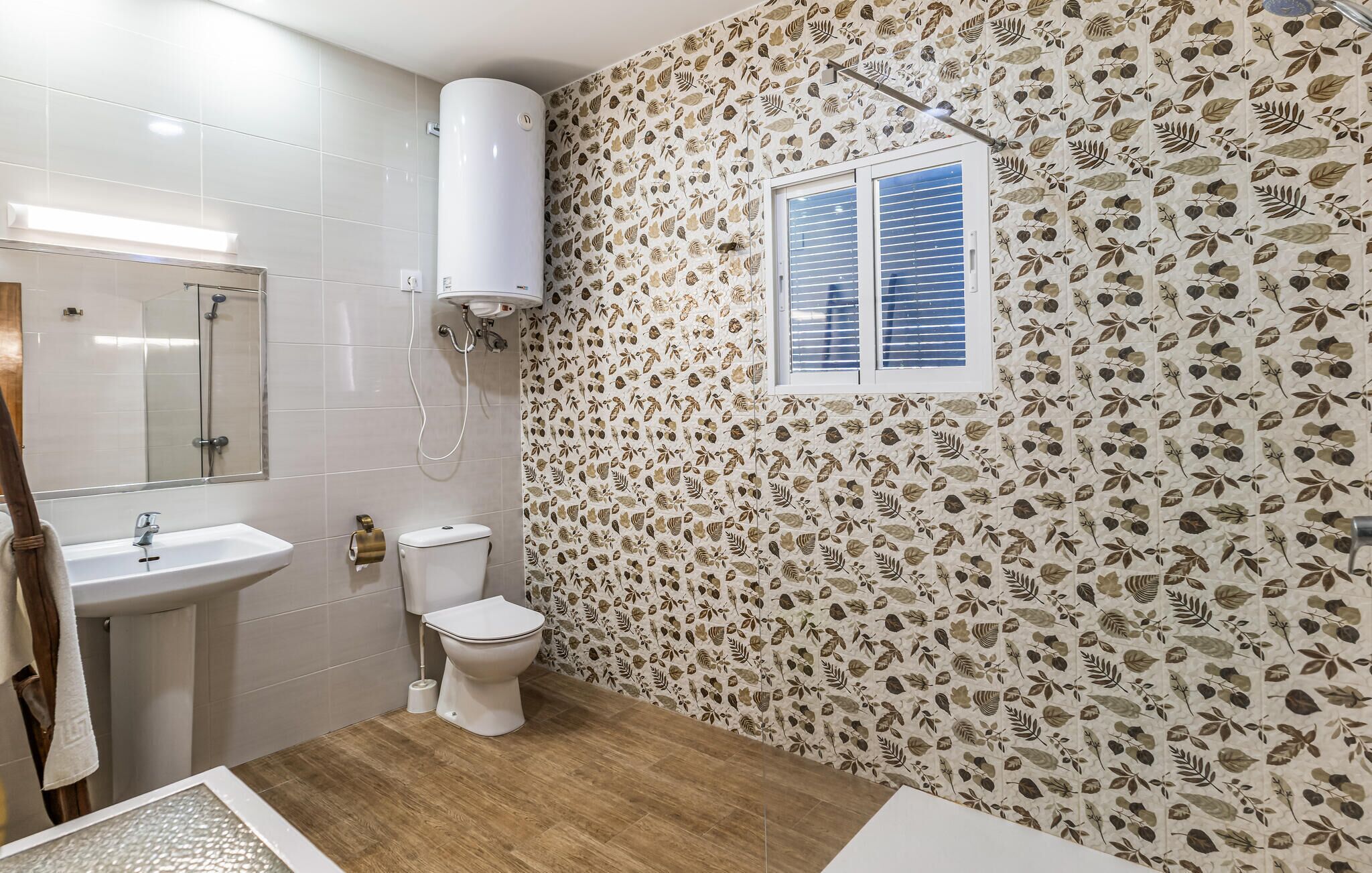 A bathroom with a toilet, sink, and shower. The walls have a leaf pattern wallpaper.
