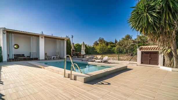 Une piscine avec une terrasse ensoleillée, des chaises longues et un espace salon couvert.