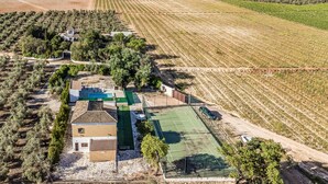 Vue aérienne d’une propriété rurale comprenant des oliveraies, un court de tennis et une petite maison avec une piscine.