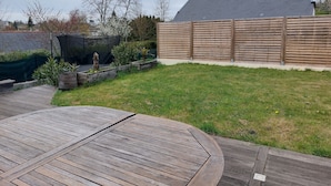Ein Garten mit einer Holzdiele, einer grünen Rasenfläche, einem Holzzaun und einem Haus mit grauem Dach.