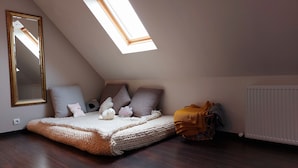Ein gemütliches Schlafzimmer im Loft-Stil mit schrägem Dach, einem Oberlicht, einem großen Spiegel und einem Bett mit vielen Kissen und einer gestrickten Decke.